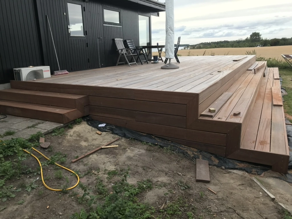 Træterrasse med indbyggede trin foran sort husfacade med havemøbler