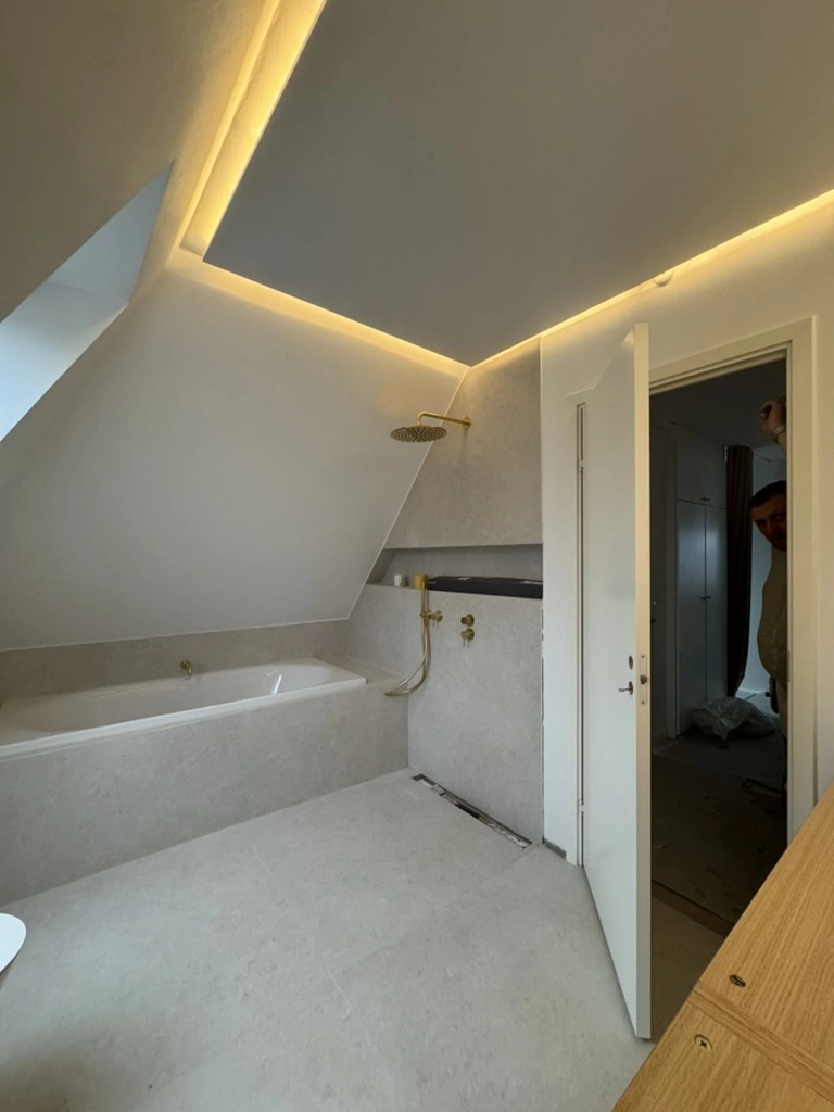 Renovering af badeværelse med store fliser, badekar under skråloft, regnbruser og indbygget LED-lys