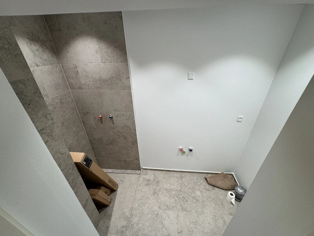 Vådrum under renovering med store grå gulv- og vægfliser og rørtilslutninger, Fliser badeværelse
