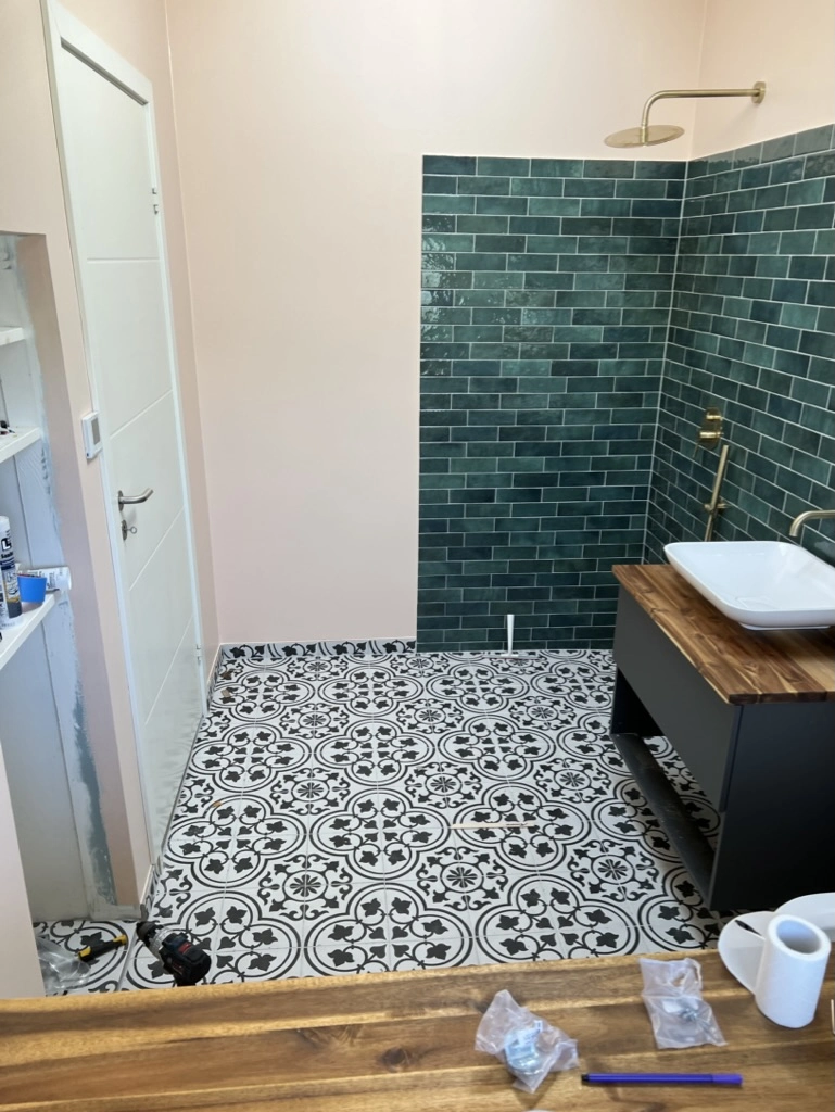 Renovering af badeværelse med nye mønstrede gulvfliser, grønne vægfliser og træbordplade med håndvask