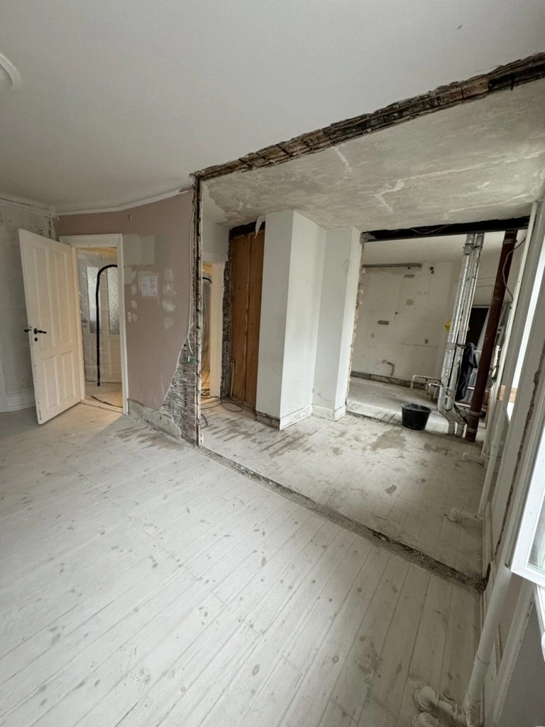 Pågående lejlighed renovering med fjernet vægsektion, eksponeret undergulv og åben rumfordeling