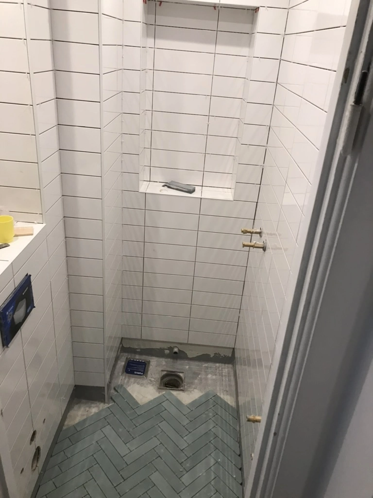 Smalt badeværelse under renovering med hvide vægfliser og mørk sildebensbelægning på gulv, Fliser badeværelse
