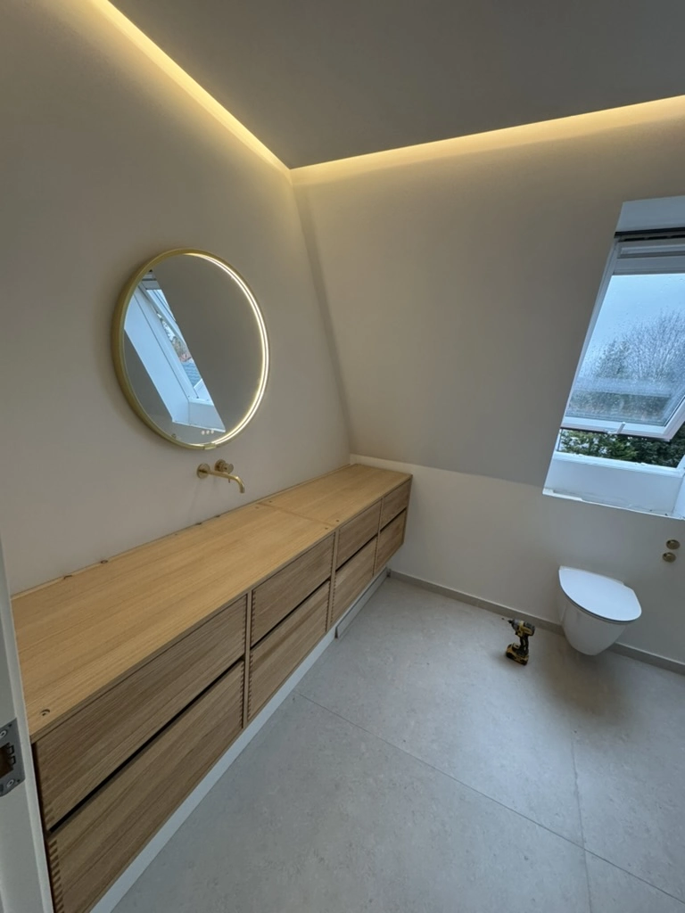 Renovering af badeværelse med træskab, rundt LED-spejl og væghængt toilet