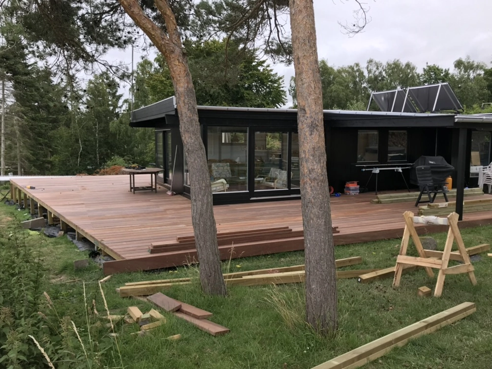 Træterrasse under opførelse ved moderne hus, med synlige terrassebrædder, byggematerialer og træarbejde