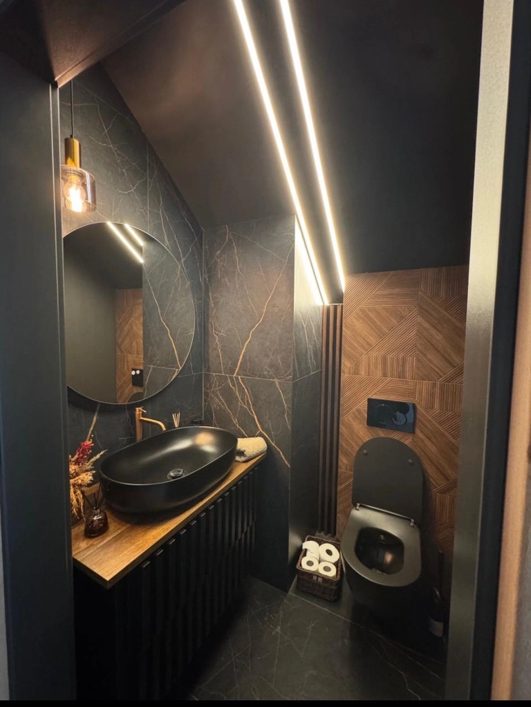 Moderne mørkt bad med sort vask og toilet, trælignende vægpaneler og LED-belysning – Renovering af badeværelse