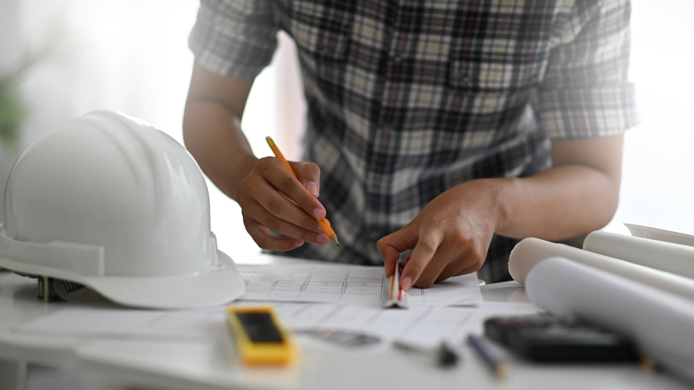 Planlægning af renovering af badeværelse med skitse, lineal, hjelm og rullede tegninger på bord