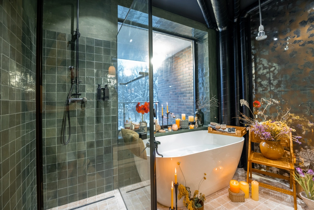 Lyst vådrum med glasbruseniche, grønne vægfliser, fritstående hvidt badekar, stearinlys og naturdetaljer. Renovering af badeværelse