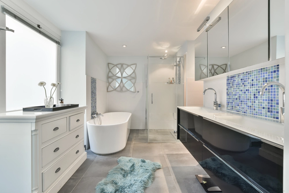 Renovering af badeværelse med fritstående badekar, glasbrusekabine, dobbelte vaske og blå mosaikfliser
